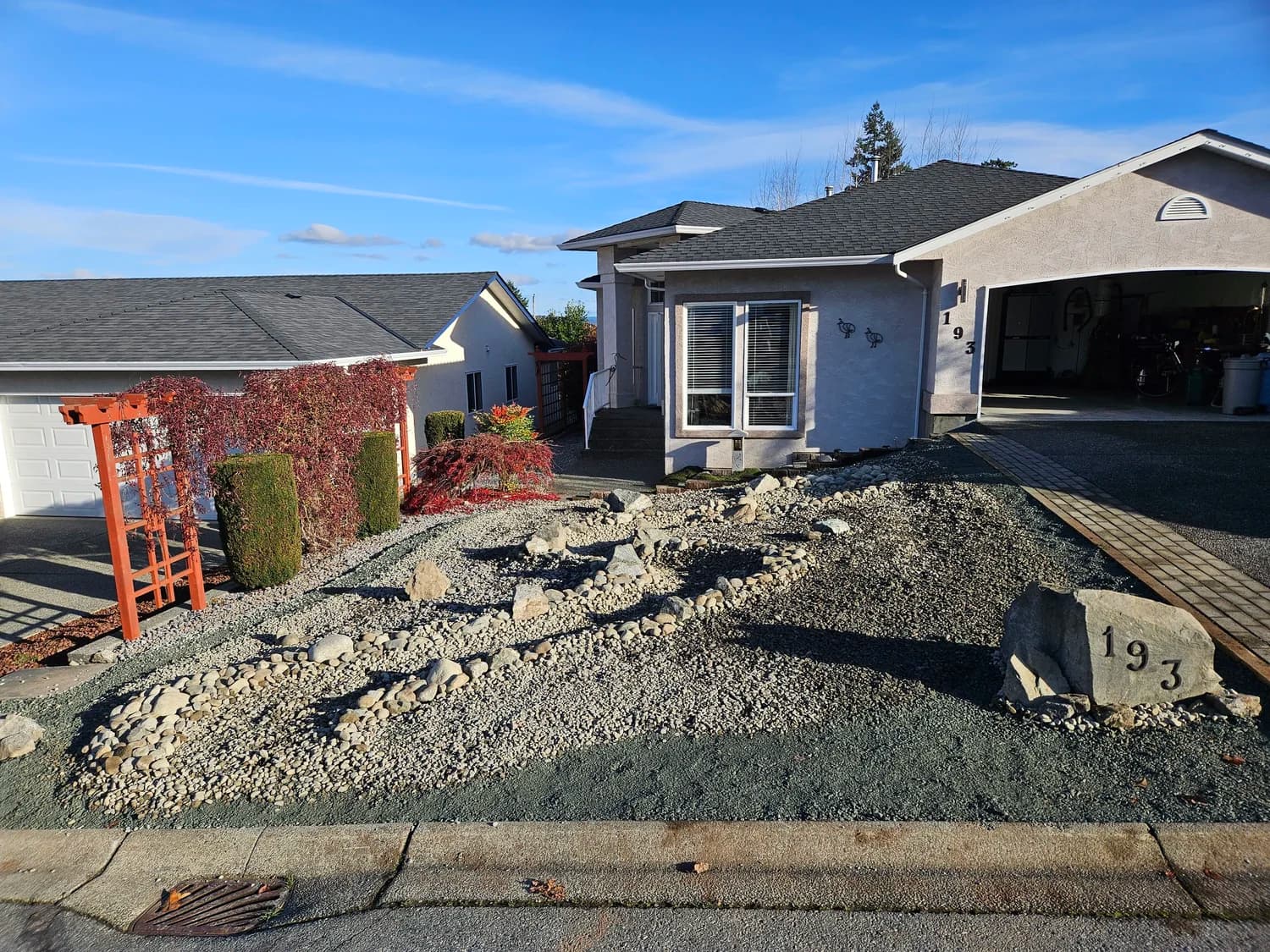 Front yard with gravel, large rocks and a red trellis beside a Japanese maple