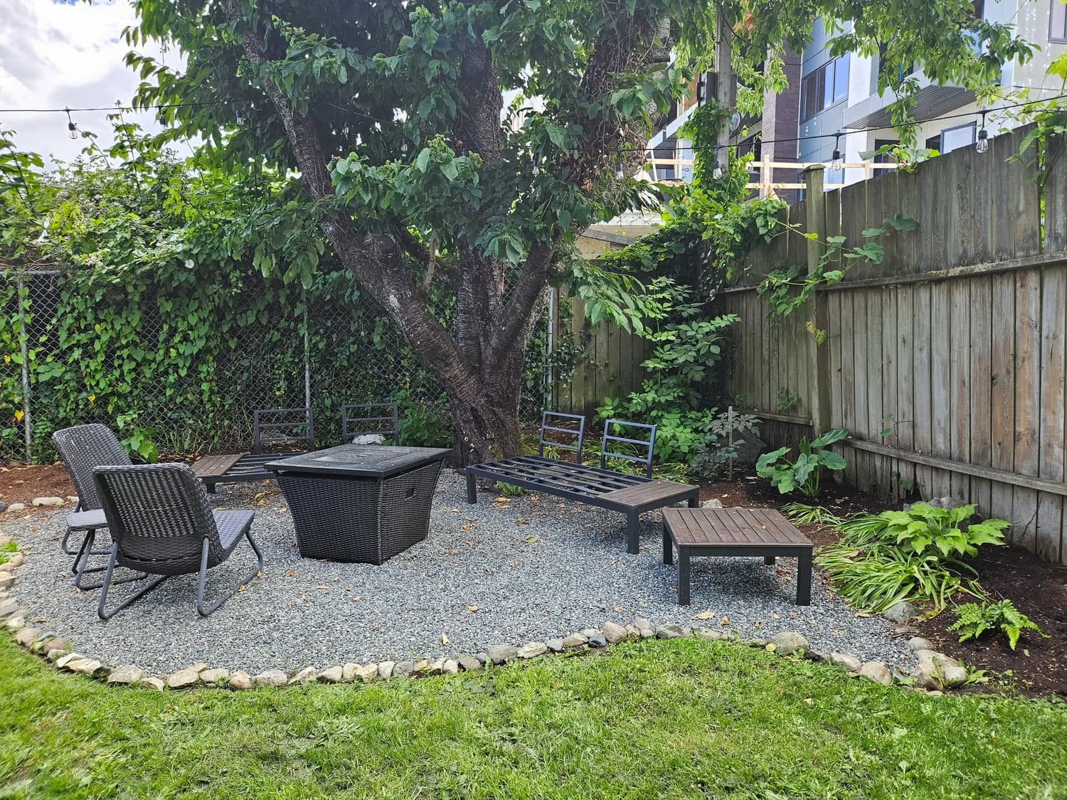 Circular gravel patio with fire pit, outdoor seating and lush garden surroundings