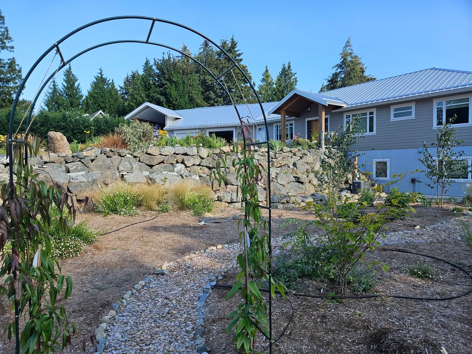 Garden arch with gravel path and large dry-stack rock wall beside a new home